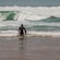 A surfer standing on a beach with his back turned and holding a surfboard